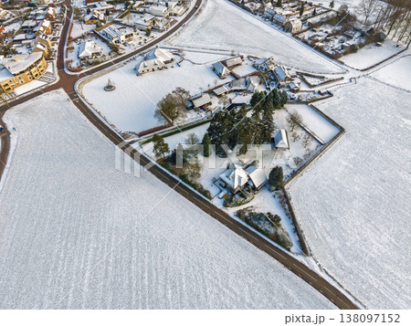 Top down aerial view of a snowy suburban neighborhood and frost covered fields. A clean winter landscape featuring modern houses, garden plots, and a long road slicing through the white terrain. Top down aerial view of a snowy suburban neighborhood and frost covered fields. A clean winter landscape featuring modern houses, garden plots, and a long road slicing through the white terrain. 138097152