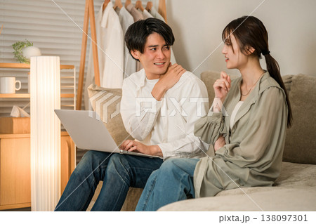 リビングのソファでパソコンで仕事をする夫を心配そうに見つめる妻(残業,持ち帰り残業,隠れ残業) リビングのソファでパソコンで仕事をする夫を心配そうに見つめる妻(残業,持ち帰り残業,隠れ残業) 138097301