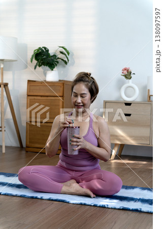 Smile woman in yoga dress sit on yoga mate Drink water to relax 138097597
