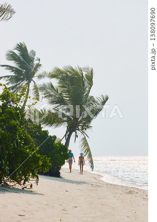 A beautiful tanned girl in a swimsuit and men walking along the white beach at sunset in the Maldives, they are happy, posing for a photographer 138097690
