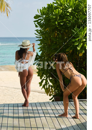 Two beautiful tanned girl friends in a swimsuit taking pictures of each other, along a white beach at sunny day in the Maldives, she is happy, she is posing 138097707