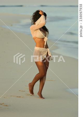 A beautiful tanned girl in a swimsuit runs along a white beach at sunset in the Maldives, she is happy, posing for a photographer 138097938