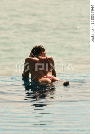 A beautiful tanned girl with an athletic physique in a swimsuit is at the edge of the pool of the villa pool on a sunset in the Maldives, she is happy and posing A beautiful tanned girl with an athletic physique in a swimsuit is at the edge of the pool of the villa pool on a sunset in the Maldives, she is happy and posing 138097944