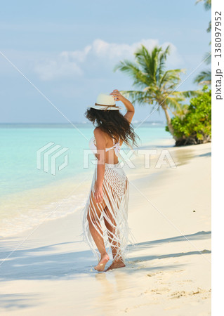 A beautiful tanned girl is wearing a hat and swimsuit with an athletic physique stands on the beach of the villa on a sunny day in the Maldives, she is happy and posing 138097952