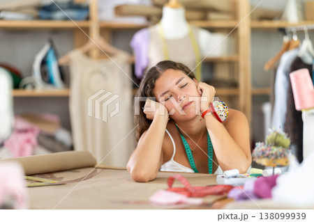 Tired female fashion designer sleeping at worktable in sewing studio Tired female fashion designer sleeping at worktable in sewing studio 138099939