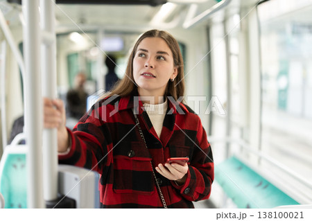 Girl is standing with phone in tram car, getting to work Girl is standing with phone in tram car, getting to work 138100021