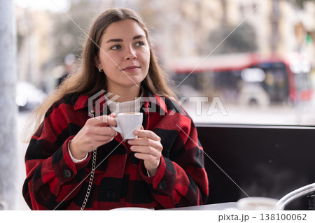 Girl in plaid jacket sits at table in street cafe, drink tea 138100062