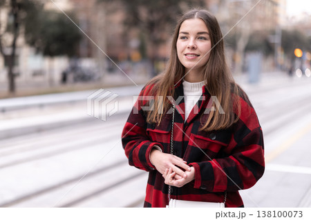 woman stands at a public transport stop 138100073