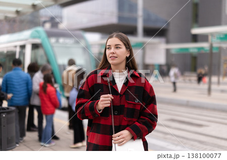 Woman standing at a tram stop 138100077