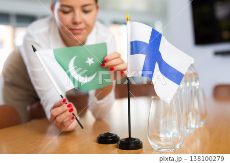 Woman secretary prepares an office for negotiations - she places flags of Finland and Pakistan table 138100279
