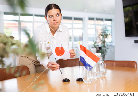 Young woman putting Japan and Netherlands flags on table in office Young woman putting Japan and Netherlands flags on table in office 138100461