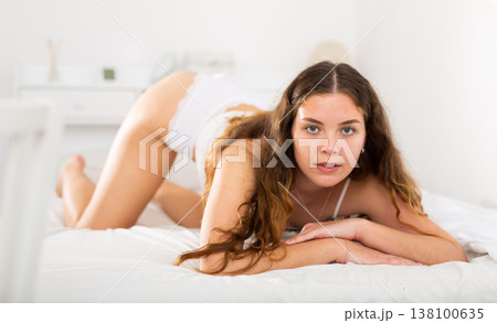 Long-haired young brunette in lingerie lying on bed 138100635