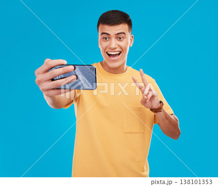 Man, selfie and peace hand sign with happiness, excited with social media with communication on blue background. V emoji, influencer with memory and smile in picture with photography in a studio Man, selfie and peace hand sign with happiness, excited with social media with communication on blue background. V emoji, influencer with memory and smile in picture with photography in a studio 138101353