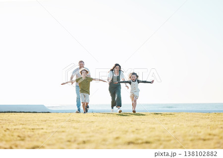 Running, parents and children on grass by ocean for bonding, relationship and relax together. Nature, travel and happy mother, father and kids on holiday, summer vacation and playing for freedom 138102882