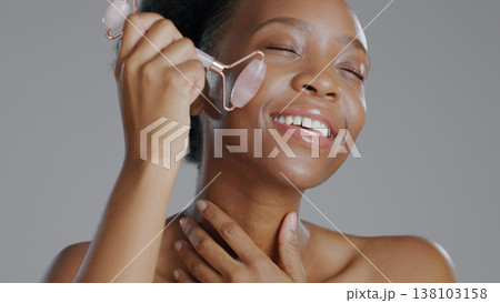Black woman, face with roller and massage for skincare and beauty, natural cosmetics and treatment on white background. Wellness, dermatology and skin glow, rose quartz crystal and tools in studio Black woman, face with roller and massage for skincare and beauty, natural cosmetics and treatment on white background. Wellness, dermatology and skin glow, rose quartz crystal and tools in studio 138103158