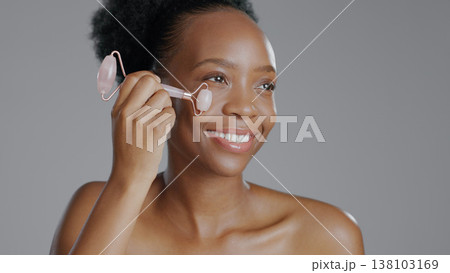 Facial roller, woman and smile in face massage in skincare or beauty, health and wellness or dermatology. Happy black person, skin and cosmetics with glow, care and tool in studio by gray background Facial roller, woman and smile in face massage in skincare or beauty, health and wellness or dermatology. Happy black person, skin and cosmetics with glow, care and tool in studio by gray background 138103169