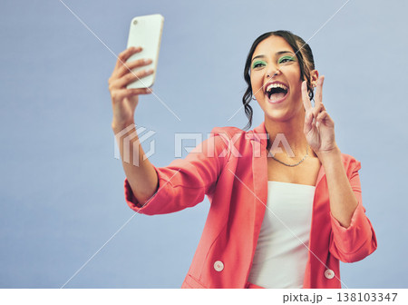 Smile, selfie and happy woman with a peace sign from social media and profile picture for creative job in studio. Influencer and makeup with career fashion with blue background and emoji hand gesture Smile, selfie and happy woman with a peace sign from social media and profile picture for creative job in studio. Influencer and makeup with career fashion with blue background and emoji hand gesture 138103347