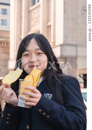 小江戸・川越のレトロな建物を背景に、名物の芋チップスを楽しむ制服姿の女子学生 138105098