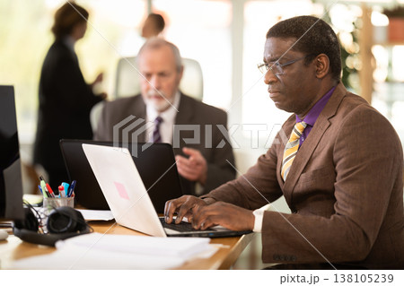 African man sitting at desk is working on laptop computer. Working day in office 138105239