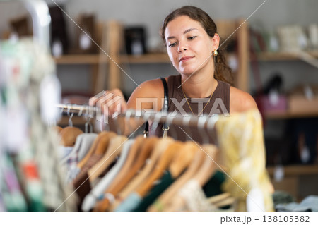 Young woman comes to boutique and looks at clothes Young woman comes to boutique and looks at clothes 138105382