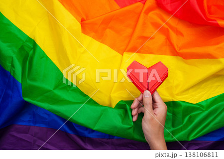 Hand holding red origami heart on rainbow flag 138106811