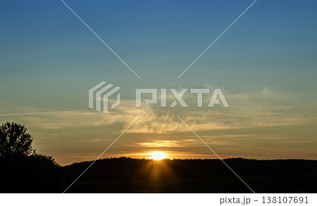 Vibrant sunset seen over rolling hills with soft clouds creating a serene atmosphere in the early evening sky Vibrant sunset seen over rolling hills with soft clouds creating a serene atmosphere in the early evening sky 138107691