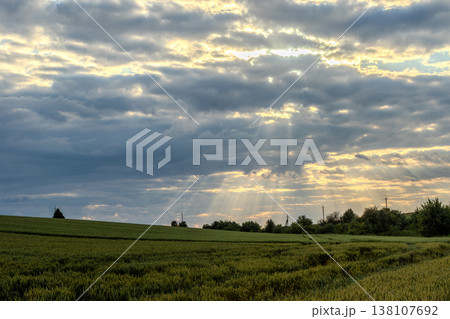 Sunlight breaks through clouds over a green landscape at dawn in a rural area 138107692