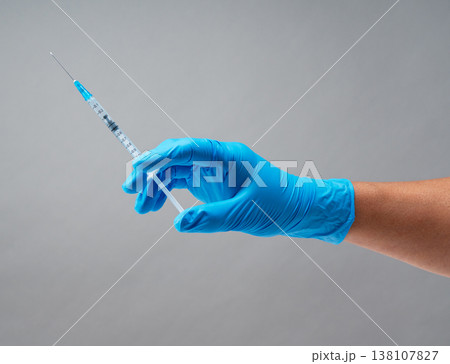グレー背景に青い医療用手袋を着用して注射器を持つ手元 138107827
