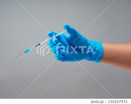 グレー背景に青い医療用手袋を着用して注射器を持つ手元 グレー背景に青い医療用手袋を着用して注射器を持つ手元 138107831