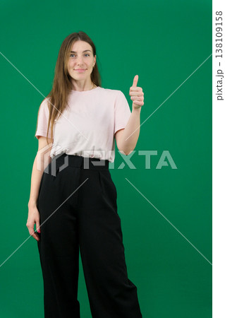 Pretty young woman showing peace gesture different emotions of a young girl on a green background chromakey beautiful facial features real people pink T-shirt white skinned European. black flared wide 138109158