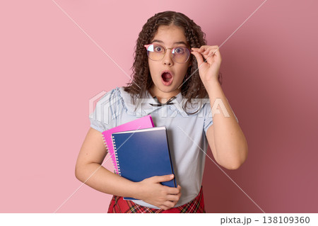 Surprised Student Holding Notebooks and Glasses with a Pink Background in a Classroom Setting Surprised Student Holding Notebooks and Glasses with a Pink Background in a Classroom Setting 138109360