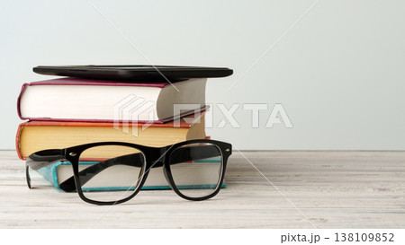 Stack of books with glasses and a tablet on a wooden table in a light room setting Stack of books with glasses and a tablet on a wooden table in a light room setting 138109852
