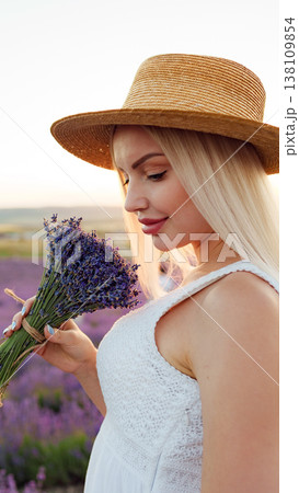 Woman holds lavender flowers in a field during sunset while wearing a straw hat Woman holds lavender flowers in a field during sunset while wearing a straw hat 138109854