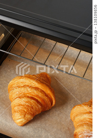 Freshly baked croissants on a baking tray in an oven set for cooking at a bakery Freshly baked croissants on a baking tray in an oven set for cooking at a bakery 138109856
