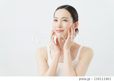 白背景の頬に手を当てる若い女性のスキンケアイメージ 138111861