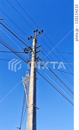 Utility pole features numerous power lines and cables against a bright blue sky, highlighting urban electrical infrastructure and connectivity 138114210