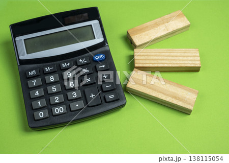 High angle view of a black calculator and three wooden blocks on a solid green background. Ideal for finance, education, planning, and accounting concepts 138115054