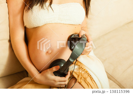 Woman with headphones on pregnant belly Woman with headphones on pregnant belly 138115396