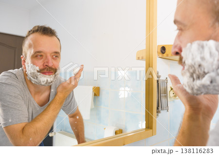 Guy shaving his beard in bathroom Guy shaving his beard in bathroom 138116283