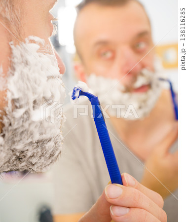 Guy shaving his beard in bathroom Guy shaving his beard in bathroom 138116285