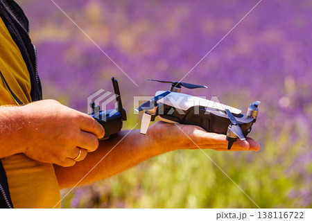 Person holds a drone in hand and remote control in the other hand while standing in a field of levender flowers 138116722