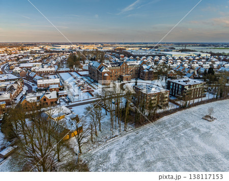 Aerial view of a historic brick building and modern residential district in a snowy Dutch landscape. Winter sunset over a European town with snow covered roofs, trees, and distant wind turbines. Aerial view of a historic brick building and modern residential district in a snowy Dutch landscape. Winter sunset over a European town with snow covered roofs, trees, and distant wind turbines. 138117153