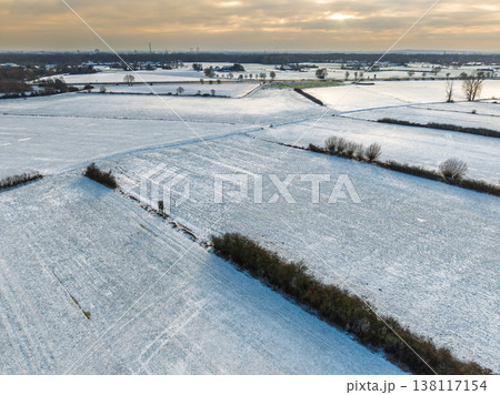 Aerial view of vast snow covered agricultural fields in the Dutch countryside at sunset. A minimalist winter landscape featuring frost, golden evening light, and a distant horizon under a hazy sky. Aerial view of vast snow covered agricultural fields in the Dutch countryside at sunset. A minimalist winter landscape featuring frost, golden evening light, and a distant horizon under a hazy sky. 138117154