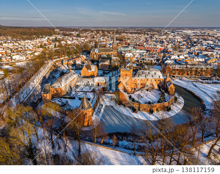 Aerial view of the medieval Huis Bergh Castle in s-Heerenberg, Netherlands. A stunning winter scene with a snow covered fortress, frozen moat, and a charming European town during golden hour. Aerial view of the medieval Huis Bergh Castle in s-Heerenberg, Netherlands. A stunning winter scene with a snow covered fortress, frozen moat, and a charming European town during golden hour. 138117159