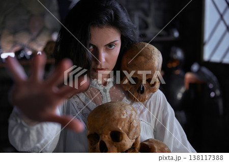 Enigmatic woman studies relic skulls in shadowed gothic room with mysterious ambiance 138117388