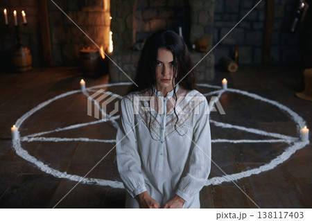 Woman practitioner in medieval chamber surrounded by candles and ancient artifacts 138117403
