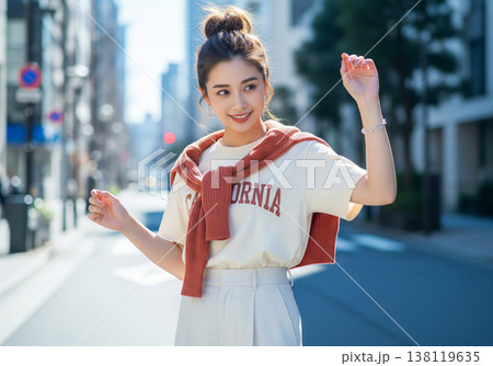 ロゴTシャツにカーディガンを肩掛けし都会を歩む女性 138119635