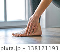 Close-up of a woman massaging her aching ankle and foot after a workout in a bright living room. 138121193