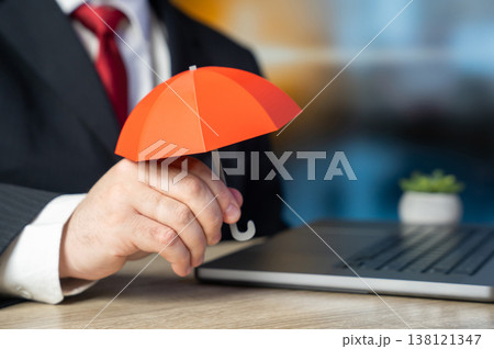 A businessman holding a red umbrella at work. Insurance and risk management. Financial protection strategies ensure stability. Corporate safety planning reduces uncertainty and supports business 138121347