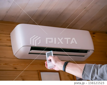 Man using remote control to turn on air conditioner mounted on wall. Person adjusting climate control settings for comfortable indoor temperature. Modern home cooling and heating system. Man using remote control to turn on air conditioner mounted on wall. Person adjusting climate control settings for comfortable indoor temperature. Modern home cooling and heating system. 138121523